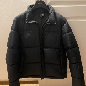 Svart pufferjacka från Everest - Säljer en svart pufferjacka från Everest. Har en klassisk pufferdesign som ger både stil och värme. Använd 3-5 gånger o inga märken. Bilder för passform finns och den är L i storleken men passar perfekt för M också.