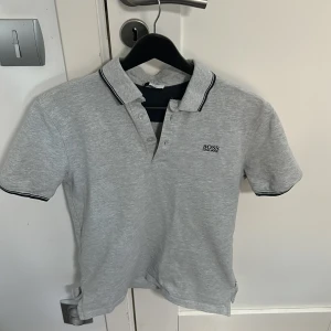 Grå pikétröja från Hugo Boss - Snygg grå pikétröja från Hugo Boss med klassisk krage och knappar. Pikén är i barn storlek 16år men hade sagt att den är i S storlek 