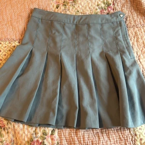 Blå kjol från Divided - Snygg blå kjol från Divided med veckad design. Perfekt för en stilren look. Har använt den kanske 1 gång, den är ungefär 44 cm lång och midjan är 38 cm