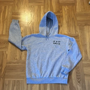 Grå hoodie med text - Säljer en grå hoodie med texten 'JE M'EN AMOUR' och en stjärna tryckt på framsidan💗Tröjan har en klassisk huva med dragsko och långa ärmar med ribbade muddar💗Den är i gott skick💗Perfekt för en avslappnad stil💗💗Säljer tröjan för 75 kr💗💗Vid intresse av tröjan hör av er💗💗