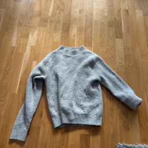 Grå stickad tröja från H&M - Säljer en mysig grå stickad tröja från H&M. Tröjan har en klassisk design med ribbstickad krage och långa ärmar. Perfekt för kyligare dagar och enkel att matcha med olika outfits.