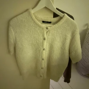 Vit kofta från Gina Tricot - Mysig vit kofta från Gina Tricot med korta ärmar och knappar framtill. Perfekt för en stilren look.
