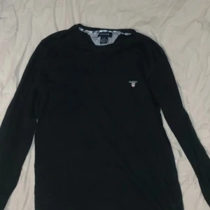 Svart långärmad tröja från GANT - Säljer en stilren svart långärmad tröja från GANT. Tröjan har en rund halsringning och ett diskret GANT-emblem på bröstet. Perfekt för en avslappnad och snygg look.