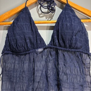 Mörkblå topp med knytband - Snygg mörkblå toppmed triangelformade kupor och knytband i nacken. Materialet är ribbat och ger en trendig look. Perfekt för en dag på stranden eller vid poolen.