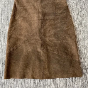 Brun mockakjol från Saint Tropez - Snygg brun mockakjol från Saint Tropez i äkta mocka. Kjolen har en klassisk A-linjeform och en diskret dragkedja i sidan. Perfekt för en stilren look. Brun mocka kjol i strl S från Saint Tropez.  Kjolen har en slits baktill och en fastsydd underkjol.  Sparsamt använd och i fint begagnat skick.  Mått Midjan: ca 38 cm Total längd: ca 63 cm  100% läder och underkjolen 100% nylon  Kommer från ett djur och rökfritt hem.