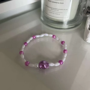 Armband med lila dödskalle - Säljer ett coolt armband med vita och lila pärlor. Armbandet har en stor lila dödskalle i mitten som ger en edgy look. Perfekt för att piffa upp din outfit!