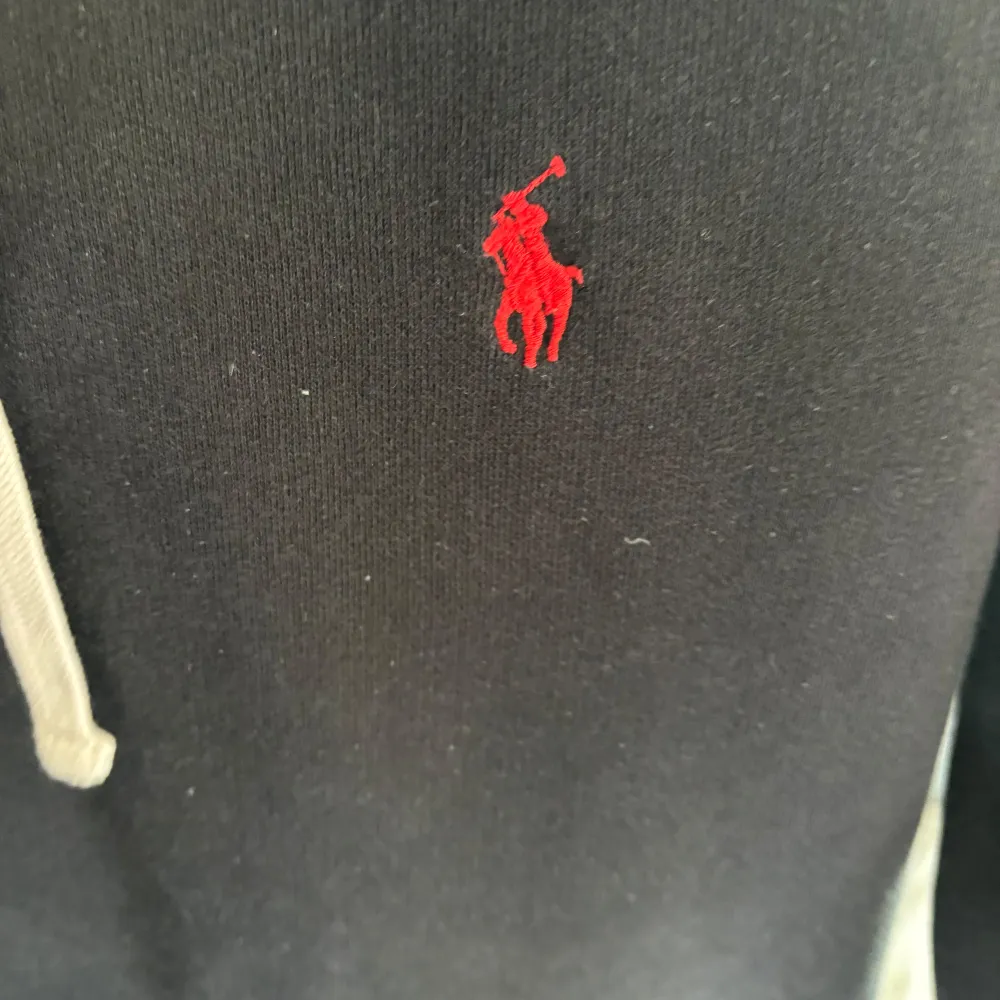 Säljer en snygg och stilren svart hoodie från Ralph Lauren. Den har en klassisk design med en röd broderad logga på bröstet och vita snören i huvan. Perfekt för både vardag och chill. Den är i bra skick och superbekväm att ha på sig. Passar perfekt till jeans eller joggers!. Tröjor & Koftor.