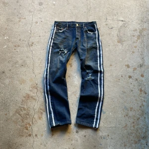 Distressed Stripe Jeans - Distressed jeans med stripes på sidorna. De är i vintage skick med distressed detaljer. Rak passform