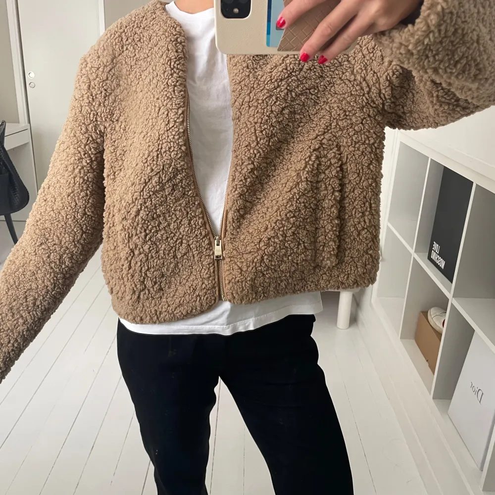 Säljer en supermysig beige teddyjacka som är perfekt för höst och vinter. Den har en dragkedja framtill och är långärmad. Jackan är croppad och ger en avslappnad look. Perfekt för att hålla sig varm och stilren samtidigt!. Jackor.