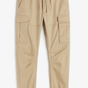 Beige cargobyxor från H&M - Säljer ett par snygga beige cargobyxor från H&M. De har en bekväm elastisk midja med snörning och stora praktiska fickor på sidorna. Perfekta för en avslappnad stil och passar till många olika tillfällen.