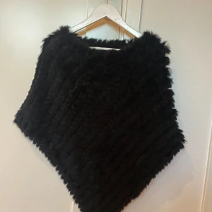 Svart poncho från Natures Collection - Säljer en supermysig svart poncho från Natures Collection. Den är gjord av 100% akryl och kaninpäls, vilket gör den både varm och stilren. Passar alla årstider, både till vardag och fest! Sparsamt använd.