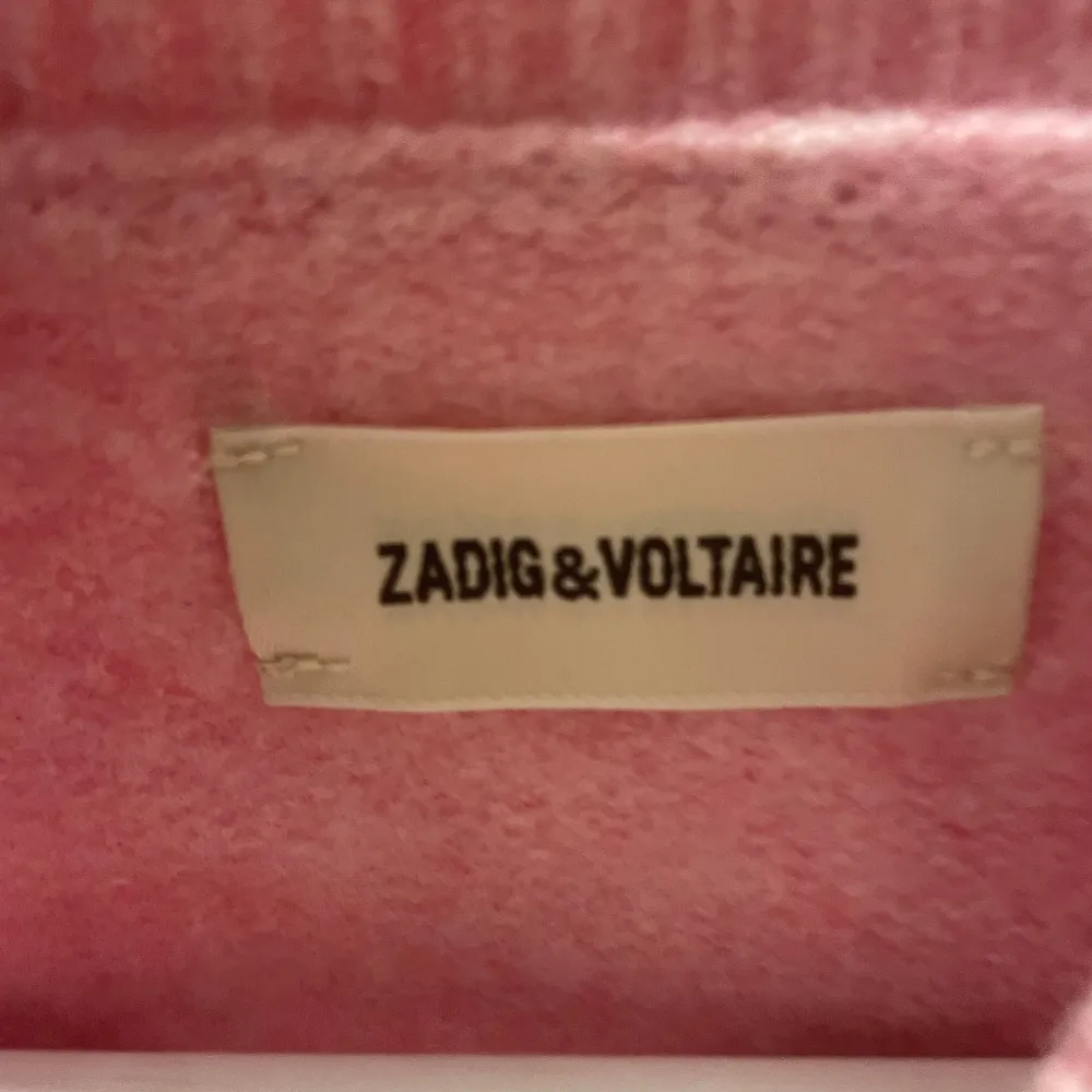 Superfin rosa stickad tröja från Zadig & Voltaire med texten 'AMOUR' i blåt på framsidan. Den har långa ärmar, perfekt för kyliga dagar. Tröjan är cool och har ribbade detaljer vid ärmslut och nederkant. Perfekt för en mysig höstl. Tröjor & Koftor.