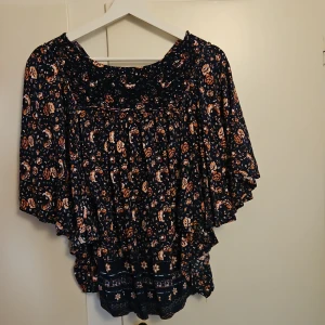 Blommig blus med vida ärmar - Säljer en superfin blommig blus med vida ärmar. Den har ett mörkt mönster med små blommor i rosa och orange. Perfekt för en bohemisk look och passar både till vardags och fest. Blusen är luftig och bekväm att bära.