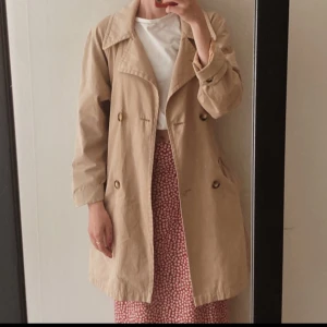Beige trenchcoat - Säljer en snygg beige trenchcoat som jag köpte på secondhand i köpenhamn med knappar framtill. Perfekt för vår och höst! Den har en klassisk krage och långa ärmar. Passar både till vardags och lite finare tillfällen.