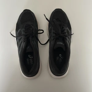 Svarta sneakers från Asics - Säljer ett par svarta Asics sneakers i bra skick. De har en snygg design med snörning och en vit sula som ger bra grepp. Perfekta för träning eller vardagsbruk.