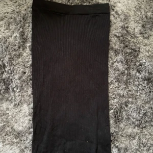 Svart ribbad kjol - Säljer en stilren svart ribbad kjol i storlek S. Kjolen är perfekt för både vardag och fest och har en skön passform. Den är enkel att matcha med olika toppar och accessoarer.