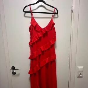 Långklänning med volanger  - Romantisk röd klänning med slits på vänster ben. Passar perfekt på resan till Spanien! Klänningen är från NA-KD och är inte använd mer än två gånger. 