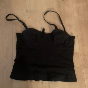 Svart korsett top - Snygg korset top ifrån Divided. Lite lösa trådar som sticker ut men inget som påverkar toppen. Hyfsat använd. Inbyggd bygel. Passar för lite mindre bröst