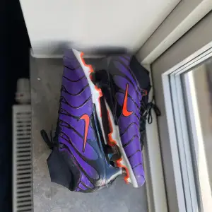 Säljer ett par coola fotbollsskor från Nike i lila och svart med orange detaljer. Skorna har en snygg design med snörning och är perfekta för fotbollsträning eller match. Sulan har en grym   greppförmåga med orangea  dobbar. Dm för fler bilder/videor