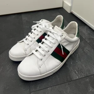 Gucci Ace - Säljer ett par snygga sneakers i storlek 43-44. Skorna är vita med de ikoniska gröna och röda ränderna på sidan. De är i bra skick med några mindre bruksspår. Passar perfekt till både vardag och fest. Tveka inte med att kontakta mig för fler frågor!😊