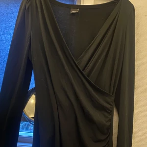 Svart omlottklänning från Gina Tricot - Säljer en elegant svart omlottklänning från Gina Tricot. Klänningen har en v-ringad design och långa ärmar, perfekt för både fest och vardag. Materialet är mjukt och bekvämt, vilket gör den idealisk för höst och vinter.