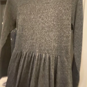 Grå långärmad klänning - Säljer en mysig grå klänning med långa ärmar. Perfekt för höst och vinter, med en bekväm passform och ett enkelt men stilrent utseende. Klänningen har en lätt rynkad detalj i midjan som ger en fin siluett.