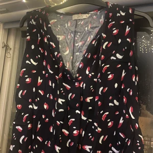 Mönstrad klänning från 365 - Säljer en snygg blus från 365 med ett coolt mönster i rött och vitt på en svart bakgrund. Blusen är ärmlös och har en bekväm passform, perfekt för både vardag och fest. Den har en v-ringad design som ger en stilren look.