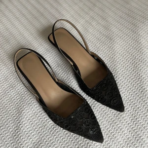 Svarta spetsiga klackskor med spetsdetaljer - Säljer ett par eleganta svarta klackskor med spetsig tå och vackra spetsdetaljer. Storlek 36 men något stora för mig som har 36 i vanliga fall, remmen åker ner från hälen för mig. Skulle därför säga att de passar 37 bättre