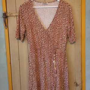 Mönstrad klänning från Stradivarius - Säljer en  peppig höstklänning från Stradivarius i storlek L men är mer som M. Klänningen har ett coolt leopardmönster i brunt och vitt, med en v-ringad hals och korta ärmar. Perfekt till boots och höstjacka.