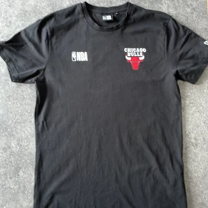 Svart Chicago Bulls t-shirt med Space Jam-tryck - Säljer en svart t-shirt med Chicago Bulls-logga på framsidan och ett coolt Space Jam-tryck på baksidan. Perfekt för basketfans! T-shirten är kortärmad och gjord i bomull, vilket gör den både bekväm och stilren. stl :S tonåring 