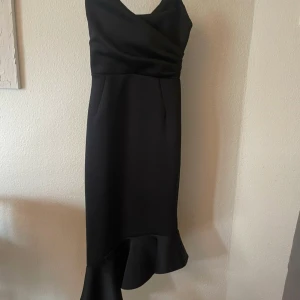 Svart klänning från Asos - Säljer en underbart vacker elegant svart klänning från Asos. Storlek M men skulle säga att den passar även S. Den har en asymmetrisk design med volangdetalj längst ner och en v-ringad urringning. Perfekt för festliga tillfällen! stretchig i materialet. Justerbara axelband. Ny och inget att anmärka på♡