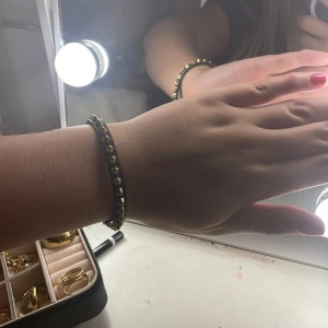 Svart armband med guldnitar från Edblad - Säljer ett snyggt svart armband från Edblad med coola guldnitar. Armbandet har en stilren design och passar perfekt för både vardag och fest. Det är i nyskick och har en enkel låsning som gör det lätt att ta på och av. Perfekt accessoar för att ge din outfit lite edge!