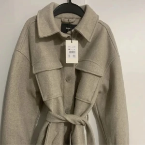 Beige kappa - Beigegrå kappa jag köpt från BikBok får något år sedan, prislappen sitter kvar och är helt oanvänd. Storleken är XS men är lite stor i storleken och kan passa upp till storlek M om man vill. 