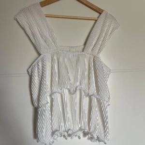 Vit blus - Säljer en superfin vit ribbad topp med breda axelband. Den har en luftig och fladdrig design med volangdetaljer längst ner. Perfekt för sommardagar eller en festlig kväll! Aldrig använd, bara testat. Nyskick