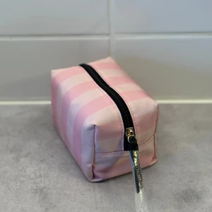 Rutig necessär från Victoria's Secret - Säljer en origil och helt ny superfin necessär från Victoria's Secret i rosa och vit rutigt mönster. myckey praktisk  och är perfekt för att förvara dina smink eller andra småsaker. Gjord i ett slitstarkt material och lätt att ta med sig på resor.