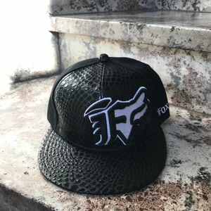 Keps - En svart keps med ”orm” mönster på. Ej justerbar och finns 3x strl: 56cm