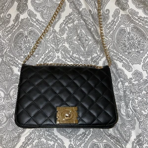 Svart handväska med gulddetaljer  - Säljer denna svarta slutsålda handväska med gulddetaljer. Som helt ny, använd fåtal gånger. Ett stort öppet fack med ett mindre fack i sidan lagom stort att lägga tex kort i. Köptes för 499kr. Säljer nu för 100kr.