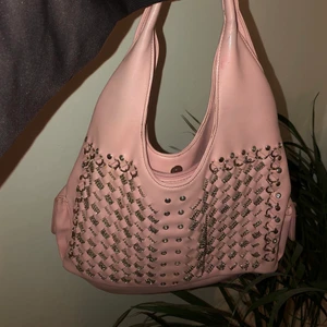 Väska - En lite mindre väska med bra utrymme i och olika fack. Ljusrosa med silvriga, coola detaljer. I bra skick.