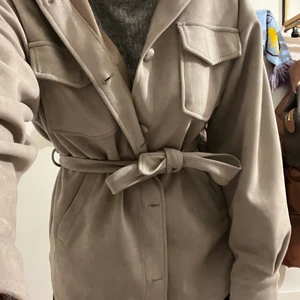 Kappa från Nelly  - Säljer min grå kappa från Nelly i storlek 38. Grå kappa med band till. Andvända en vår så i så gott som nytt skick. Knapparna sitter löst vilket de har gjort sen jag köpte och funkar fint. Säljes för 175kr hämtas i Halmstad eller skickas mot frakt 