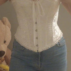 Vit spetskorsett!!  - En jättefin vit korsett som jag tyvärr tröttnat på. Den är storlek 40/42 men är justerbar i ryggen. Jag är en M och den passar perfekt. Korsetten är "äkta" med stålpinnar i. Den är inte slät utan har ett mönster som man kan se på bilderna. Är skitsnygg ovanpå en skjorta eller klänning eller bara som den är. Den är använd 1 gång och är i nyskick. 