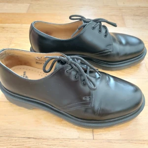 Dr. Martens svarta 1461, 39 - Dr. Martens lågskor i modell 1461, i gott skick då de endast använts ca 2 veckor förra året. Skulle säga att de är lite större i storleken än en vanlig 39 då de passar mig som oftast har 40 (går säkert att lägga in sulor dock).