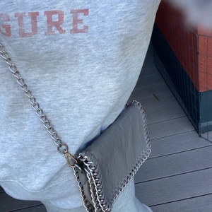 Tiamo grå liten väska  - Jag säljer en TIAMO ljus grå väska i den mindre modellen. Den har rostat lite på knäpparna, men inget man tänker på. Ordinarie pris 450kr. Köparen står för frakten. 