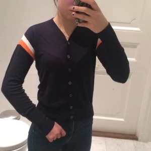 Marinblå kofta med vita och oranga ränder - Säljer denna marinblå kofta med oranga och vita ränder på överarmarna. Den är använd 1 gång och i nyskick. Den är i storlek 12 år, men skulle säga att det motsvarar storlek XS