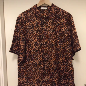 Sandro Paris damsidenskjorta stl 40 - Helt oanvänd underbar kortärmad sidenskjorta från Sandro Paris storlek 40. Plaggets längd fram:  71 cm. Bak: 79 cm. Mått över byst fram: 50 cm. Svarta knappar i pärlemor. Finns i Hammarby sjöstad. Köpt våren 2020. Nypris: 895 kr. 