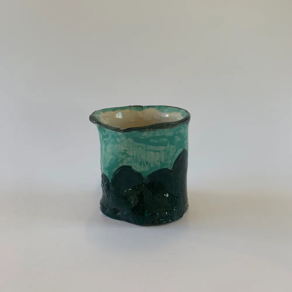 En handgjord kopp i keramik med en grön glasyr. Denna kopp saknar öra men passar dock bra i handen. . Övrigt.