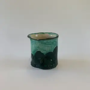 En handgjord kopp i keramik med en grön glasyr. Denna kopp saknar öra men passar dock bra i handen. 
