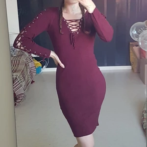 Mörkröd Vinröd tajt klänning med snörning - Mörkröd/vinröd, tajt, ribbad, skön, klänning med snörning, både vid bysten och längsmed båda ärmarna. Passar stl. 36-38. Frakt tillkommer.