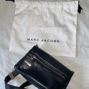 Marc Jacobs väska  - Liten men rymlig väska från Marc Jacobs. Köpt 2017 på NK i Göteborg för 4 100kr. Finns två dragkedjefack, ett inne samt ett på utsidan och två små tygfack. Axelbandet går att justera längd på. Lite slitage finns, några sminkfläckar inuti samt lite repigt på metallen, men fortfarande fint skick på den. Skickar gärna fler bilder om önskas och priset kan absolut diskuteras. Frakten är inte 100% då jag inte vet hur stort som behövs. 