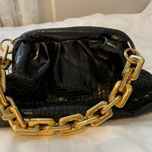 Svart väska i ormskinnsimitation - Svart lackliknande väska i likt ormskinnsmänster. Guldhantag plus ett medskickande längre handtag. Aldrig använd. 