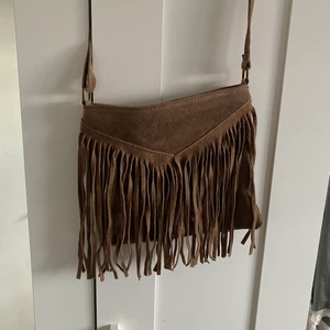 Brun axelbandsväska med fransar - Brun axelbandsväska med justerbart band. Väskan är köpt i en butik i Spanien och är aldrig använd. Den är rymlig till vardagliga saker:) köparen står för frakt.